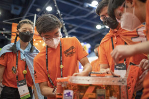 Boys and girls in orange shirts working on robots 